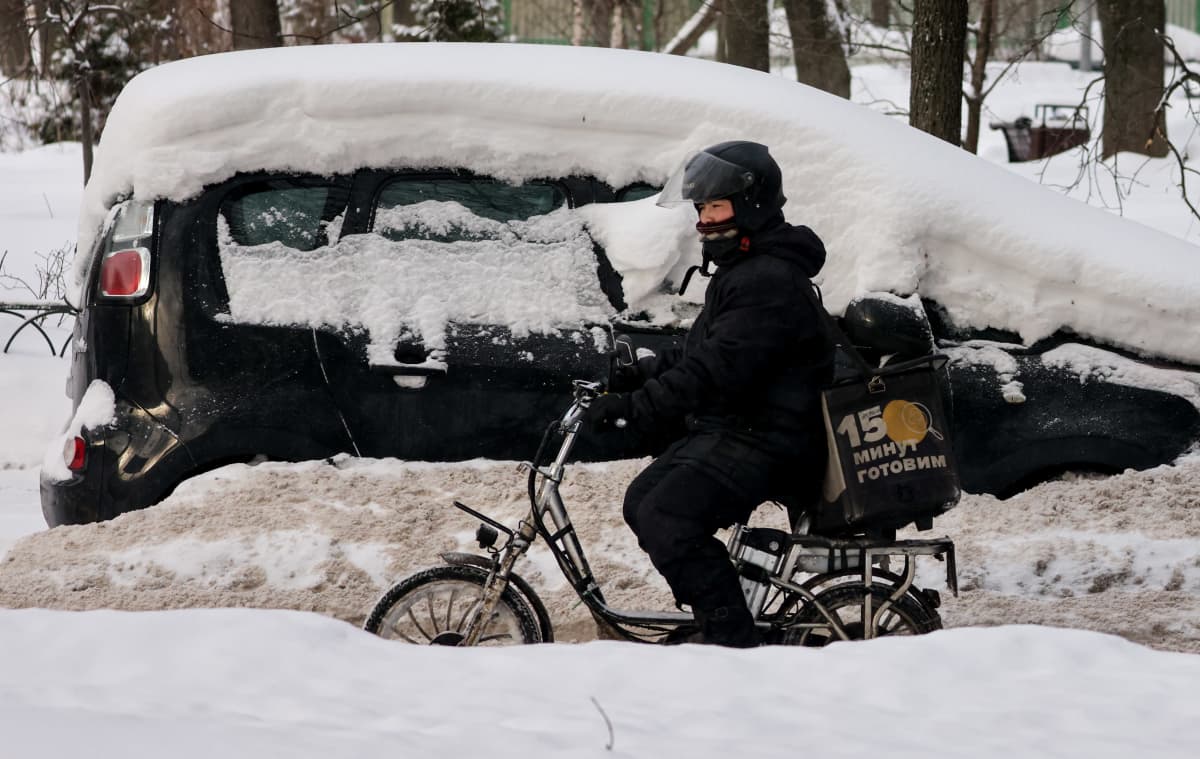 Ruokalähetti pyöräilee lumikinosten keskellä Moskovassa.