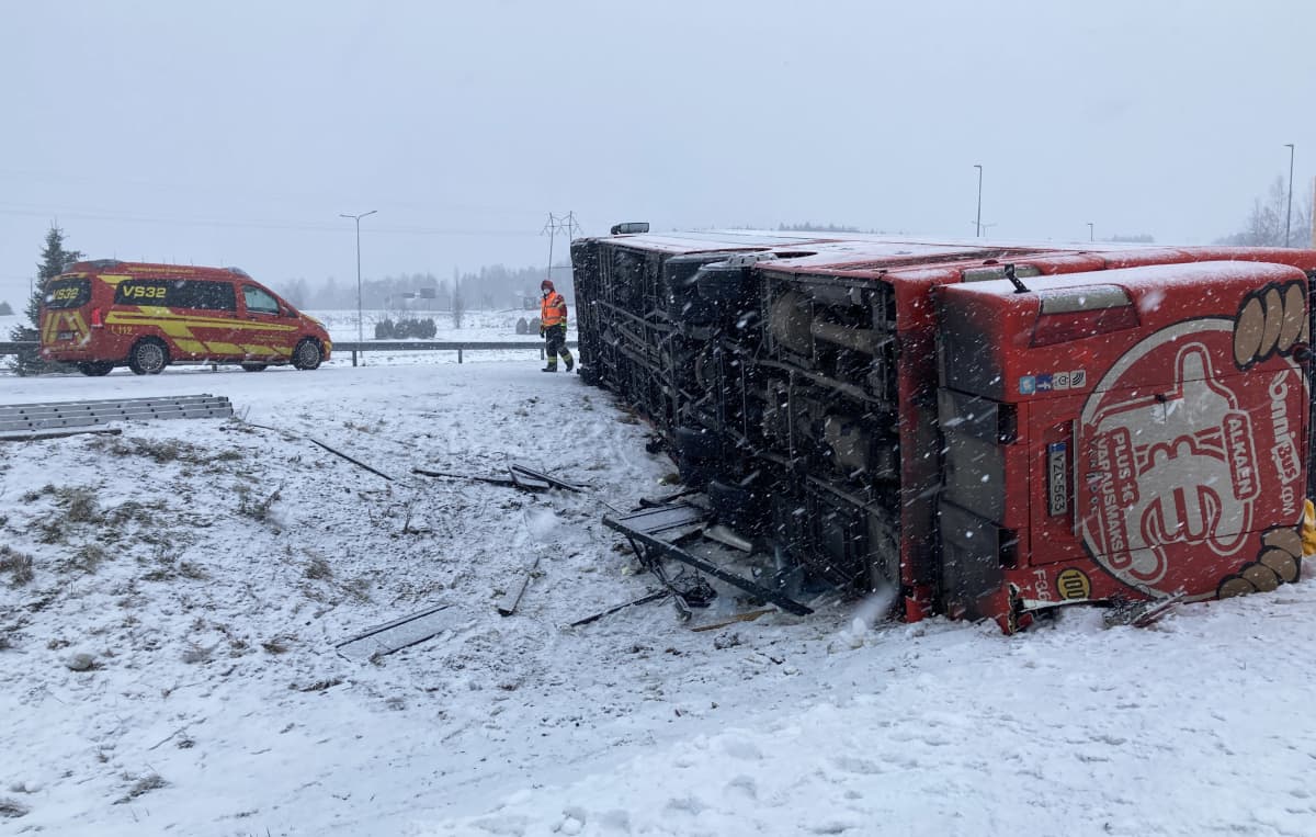Kaatunut linja-auto lumisella tien pientareella, ambulanssi ja pelastusviranomainen.