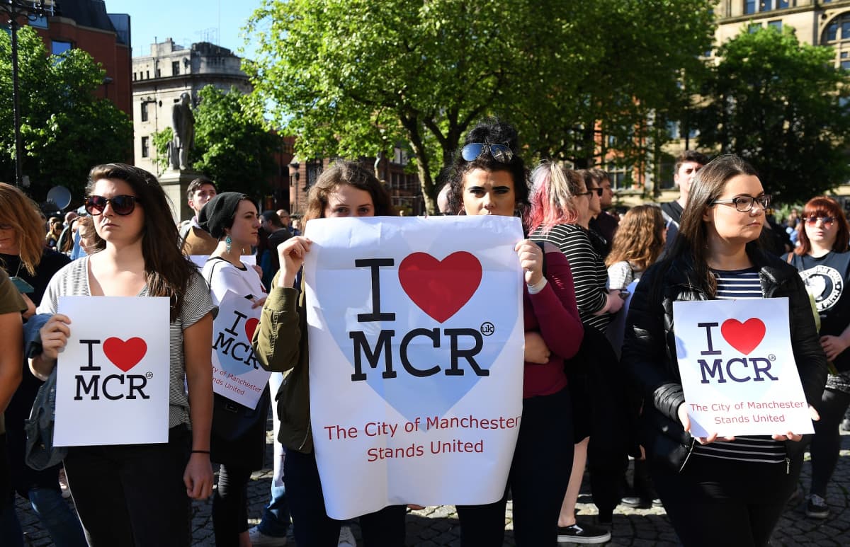 Joukko ihmisiä. Eturivissä olevilla on julisteet, joissa lukee I love MCR, The City of Manchester Stands United.