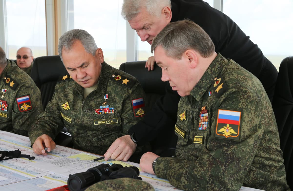 Sergei Šoigu ja Valeri Gerasimov istuvat pöydän ääressä maastokuvioisissa univormuissa ja tutkivat vakavina karttaa. Kollmas mies kurkottaa heidän välistään ja näyttää kynllä kohtaa kartasta.