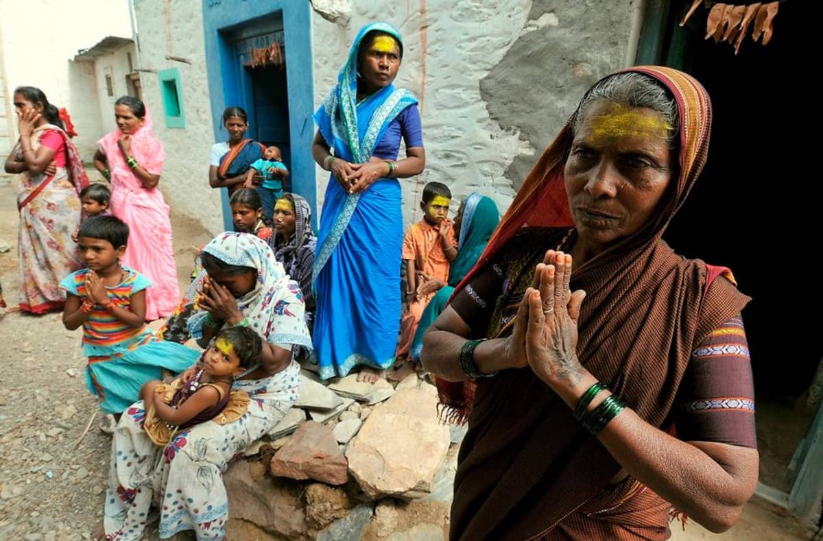 Intilaisia naisia ja lapsia kädet yhteen liitettyinä. Heidän otsansa on maalattu keltaisiksi. 