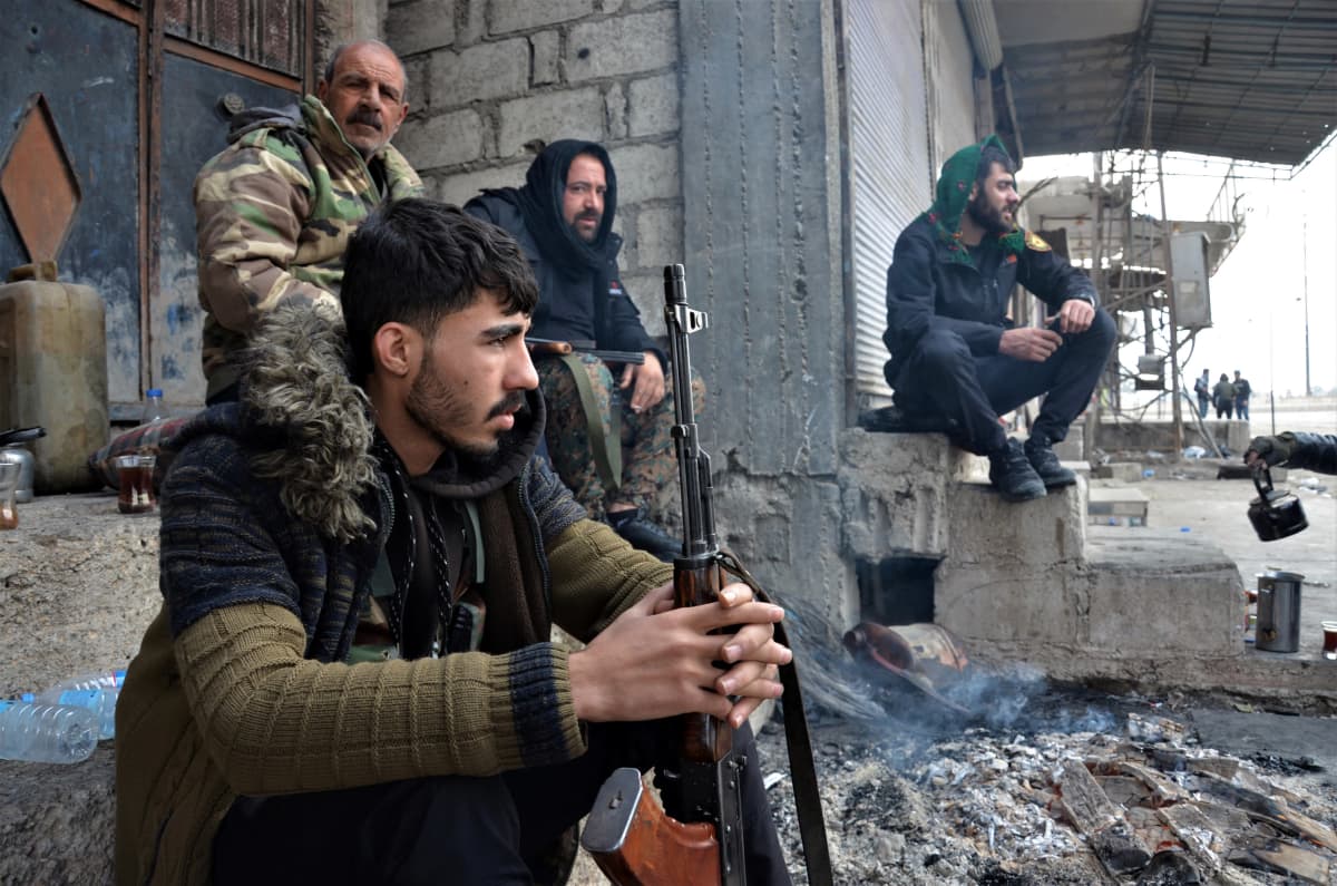 Syyrialaisia taistelijoita istumassa rakennuksen edustalla.