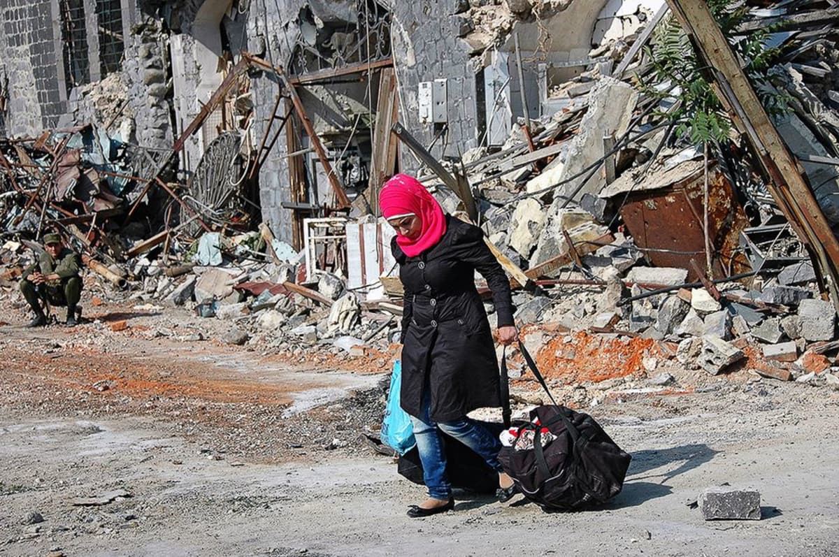 Syyrialaisnainen  raunioituneen Homsin kaupungin kadulla.