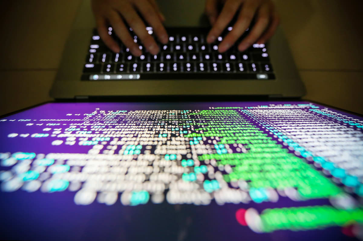 På bilden syns en datorskärm med massa kodspråk. Bilden är tagen uppifrån och man ser hur två händer skriver på tangentbordet.