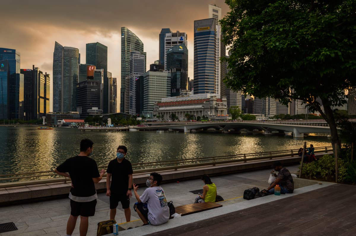 Ihmisiä veden äärellä Singaporessa. Taustalla pilvenpiirtäjiä ilta-auringossa.