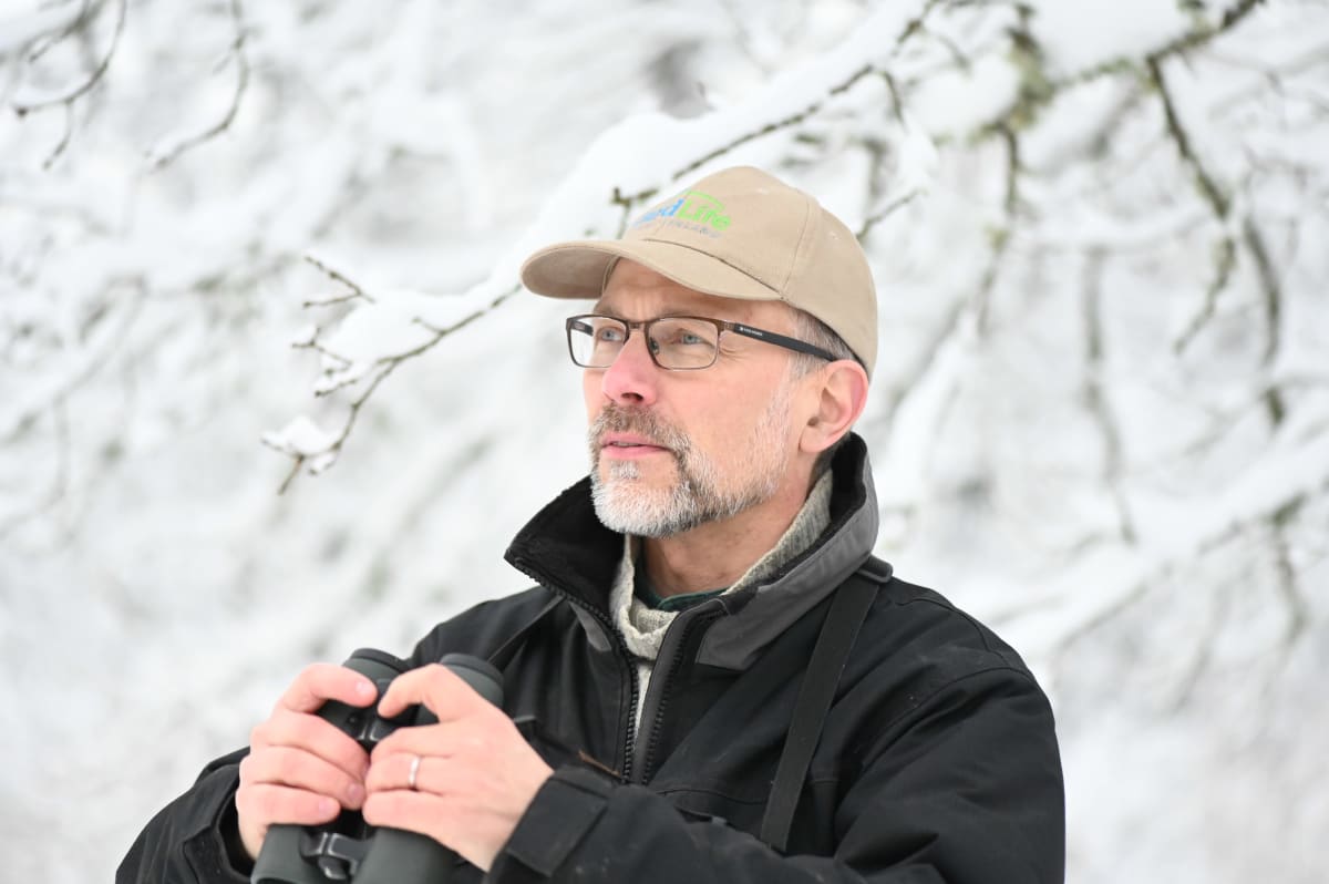 Lintuharrastaja kiikarin kanssa talvisessa luonnossa. 