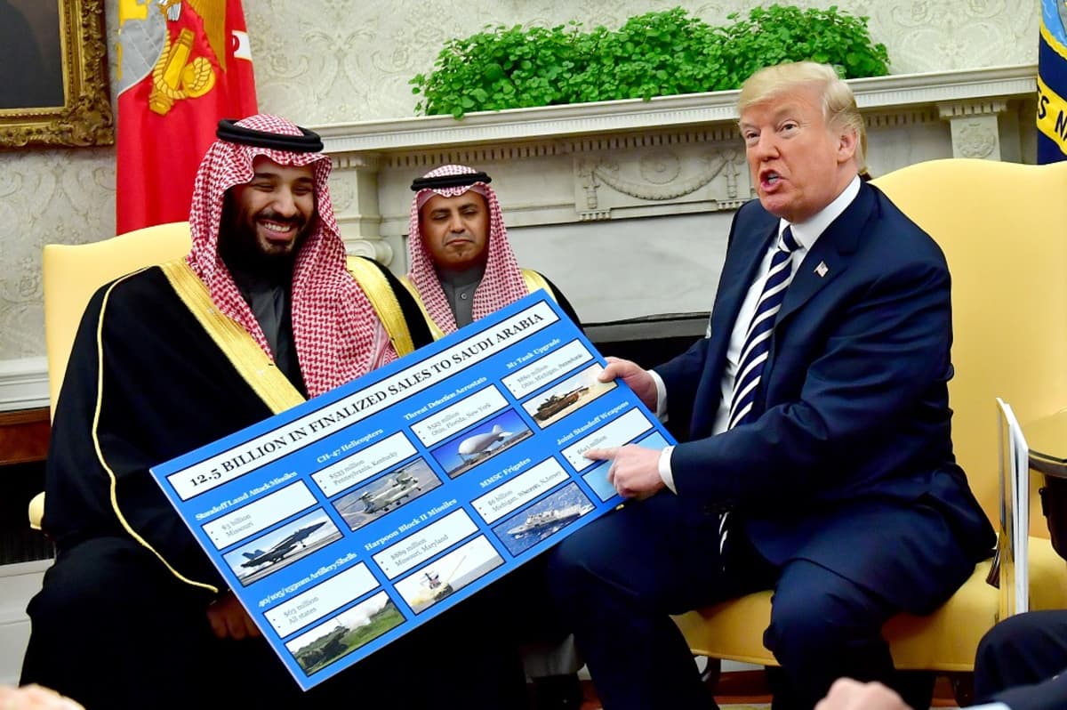 Mohammed bin Salman ja Trump istuvat tuoleilla. Trump osoittaa kädessään olevaa kuvaesitystä, jossa on kuvia muun muassa hävittäjistä ja sota-aluksista. Kruununprinssi nauraa.