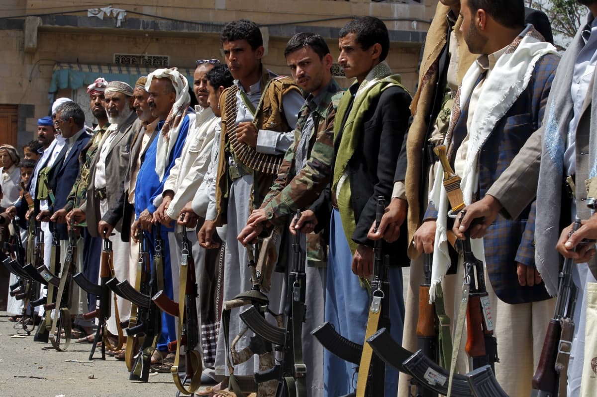 Jemenin huthikapinallisia tukevia miehiä seisoo rivissä, kiväärit maata vasten nojaten. 