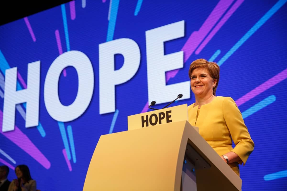 Kuvassa Skotlannin pääministeri Nicola Sturgeon lavalla puhujanpönton takana. Taustakankaalla lukee isoilla kirjaimilla teksti HOPE eli toivo. 