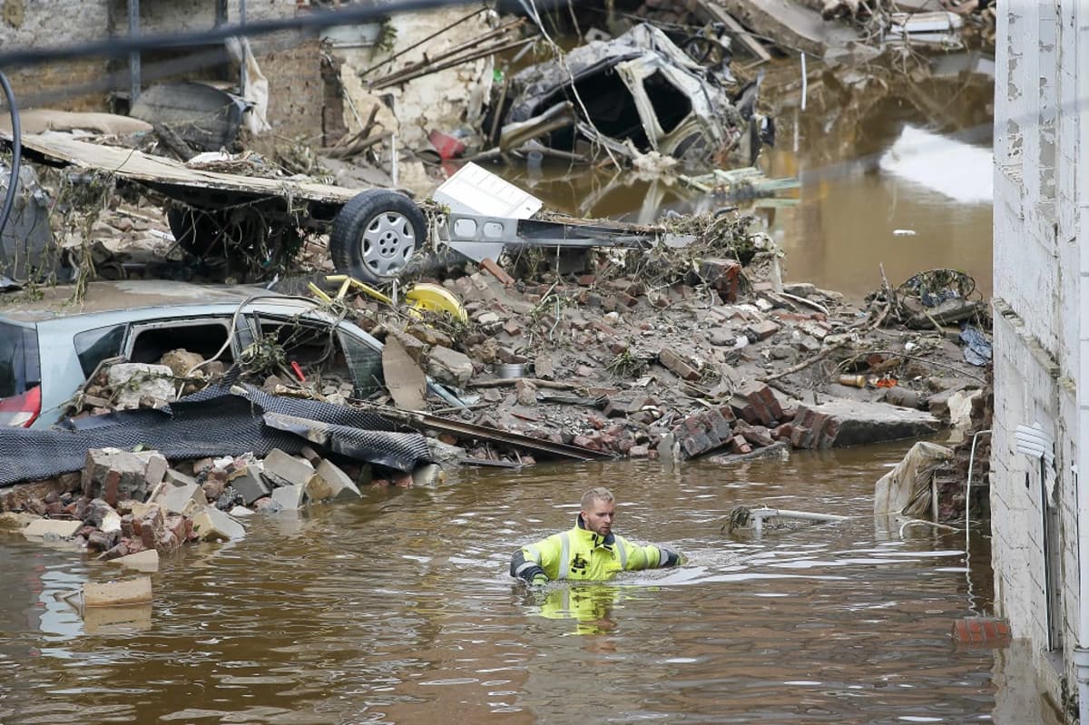 Mies kahlaa kainaloitaan myöten ruskeassa vedessä. Ympärillä täysin tuhoutuneita autoja ja muuta roimaa.