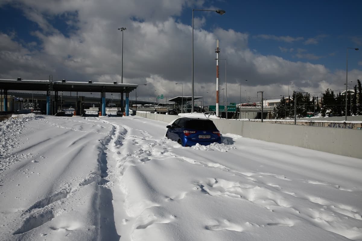 Kuvassa sininen auto lumen täyttämällä tiellä. 