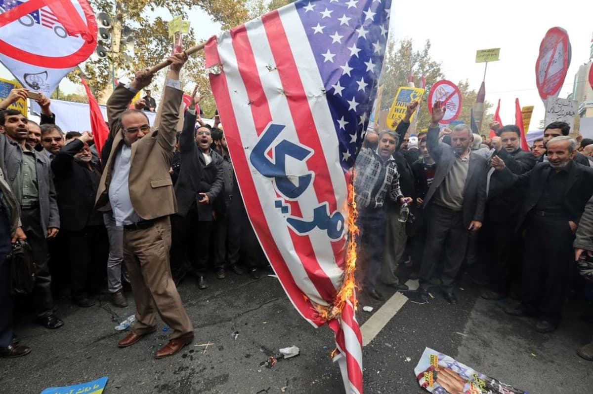 Mielenosoittaja nostaa palavaa Yhdysvaltain lippua. Taustalla suosiota osoittavia ihmisiä.