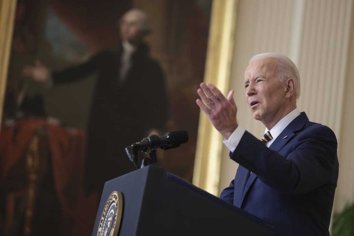Presidentti Joe Biden puhuu, taustalla taulu joka esittää jotakin entistä presidenttiä. Sekä Bidenilla että taulussa käsi tehostaa puhetta. 