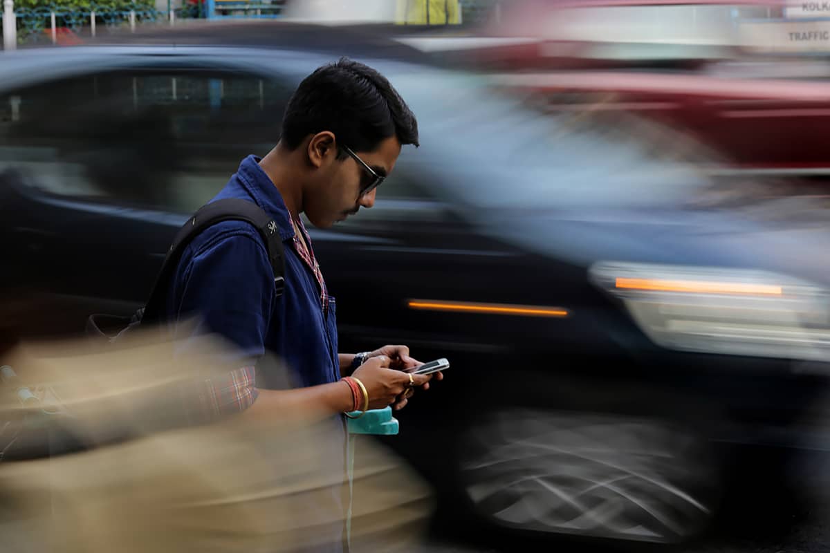 Intialainen mies näpyttelee puhelintaan kadulla.