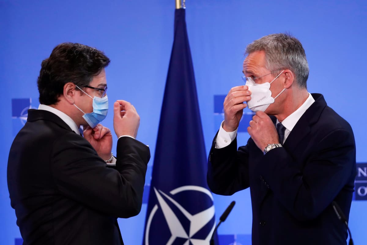 Ukrainan ulkoministeri ja Naton pääsihteeri asettavat maskeja kasvoilleen. Miehillä on tummat puvut ja kravatit. Taustalla on Naton lippu.