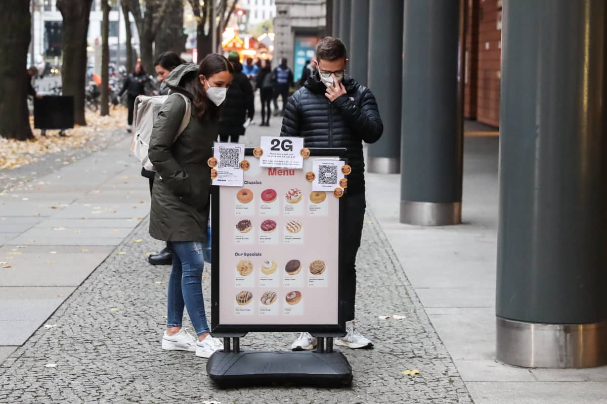 Mies ja nainen katselevat donitsikaupan kylttiä Berliinissä maanantaina. Kyltissä on kerrottu kiristyneistä koronarajoituksista.