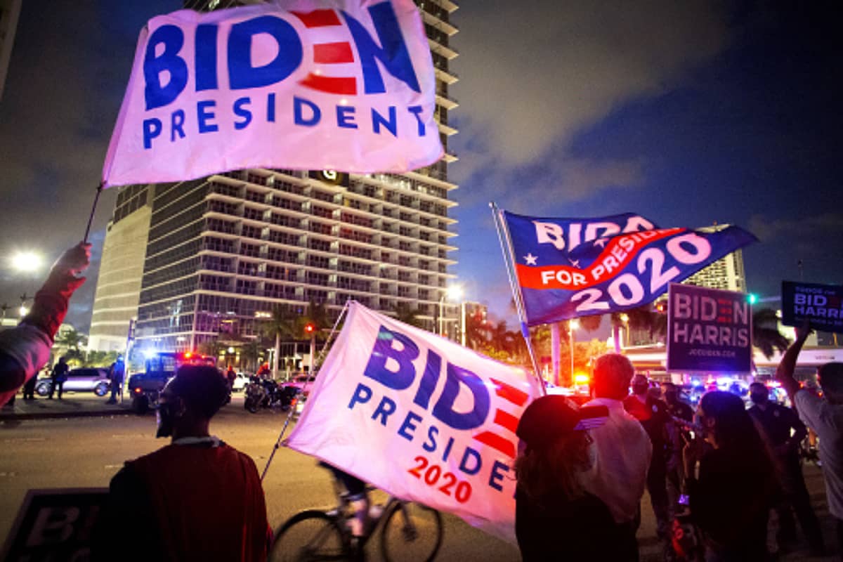 Kannattajat heiluttavat Joe Bidenia tukevia lippuja öisessä kaupunkimaisessa.