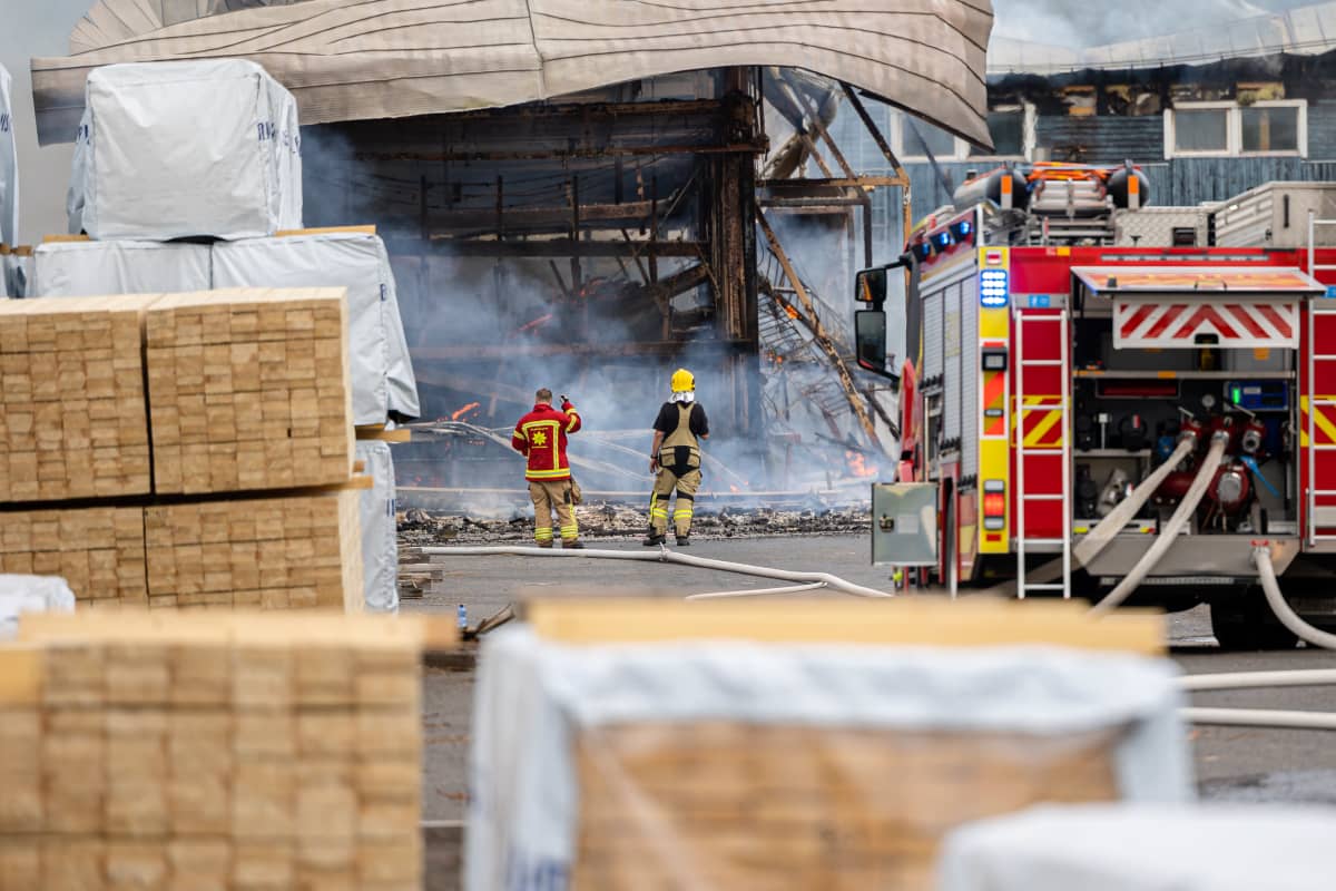 Kaksi palomiestä katsovat palossa tuhoutuneeseen varastorakennukseen Mustola Timber -sahalla Lappeenrannassa.