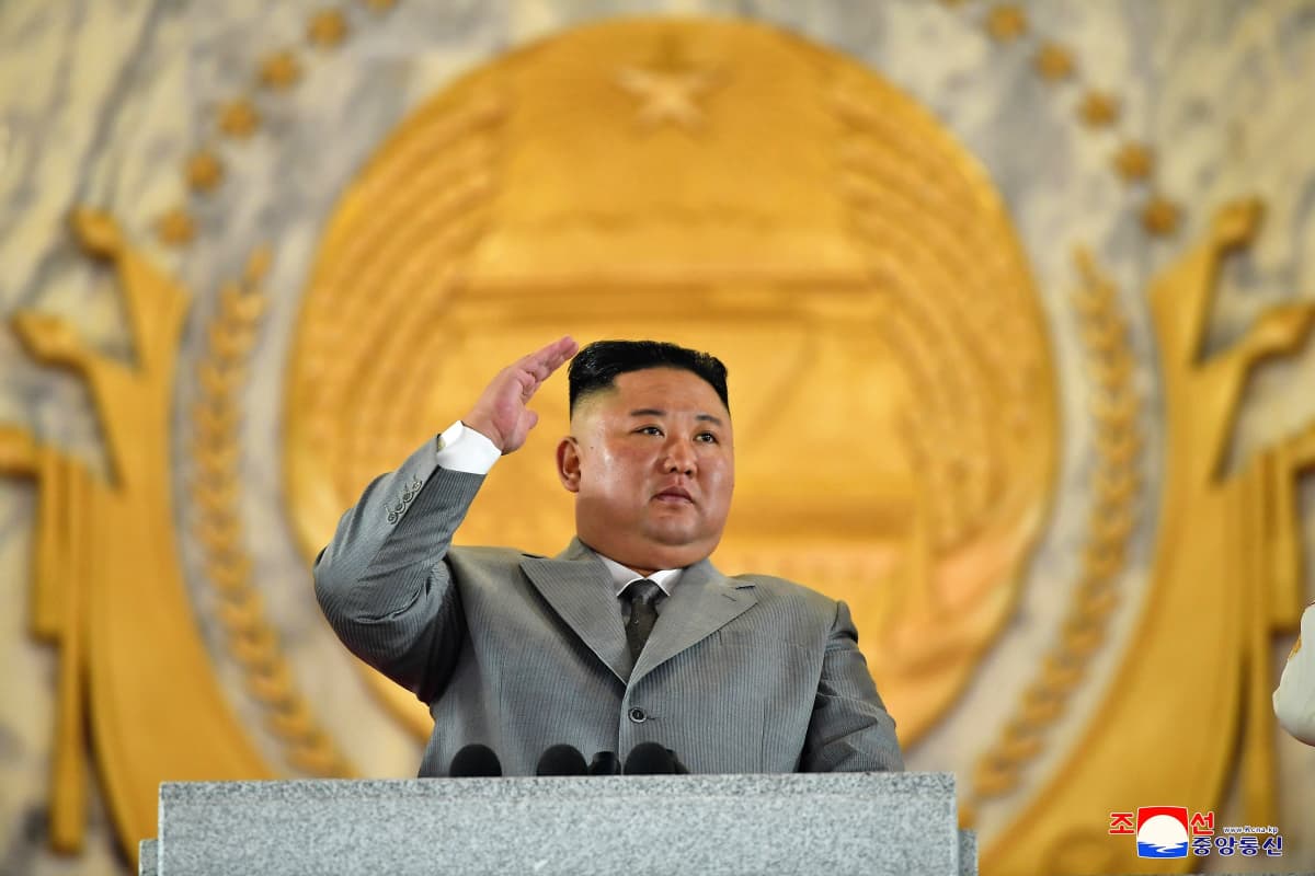 Kim Jong-un seisoo puhujanpöntön takana harmaassa puvussa ja tervehtii paraatia.