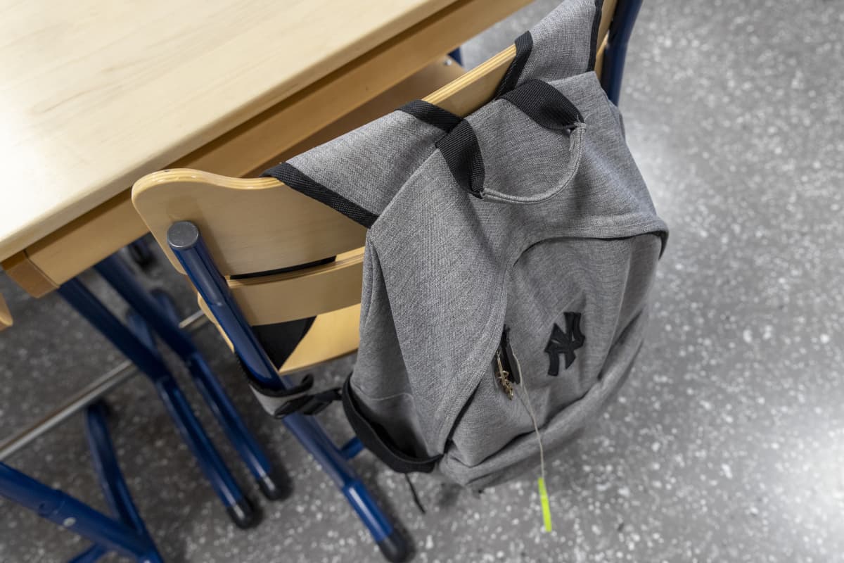 Yksinäinen koulureppu roikkuu luokassa tuolin selkänojasta.