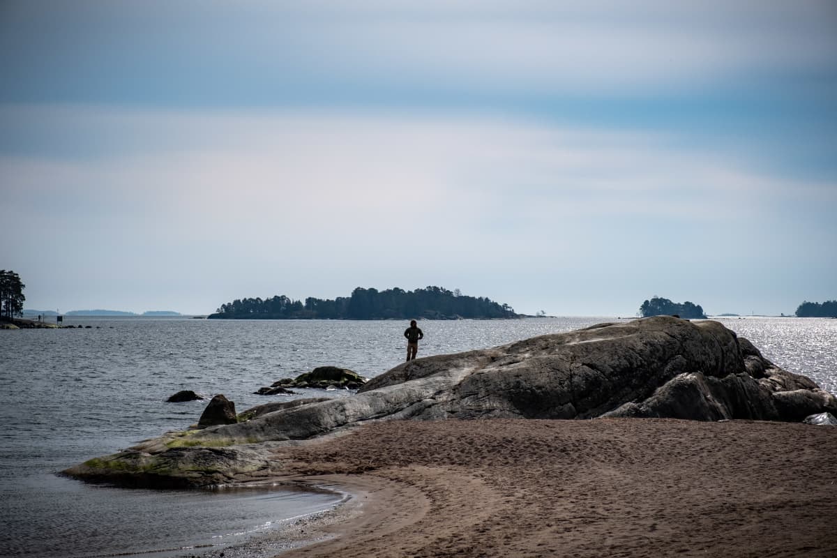 Mies seisoo rantakalliolla Aurinkolahden rannalla.