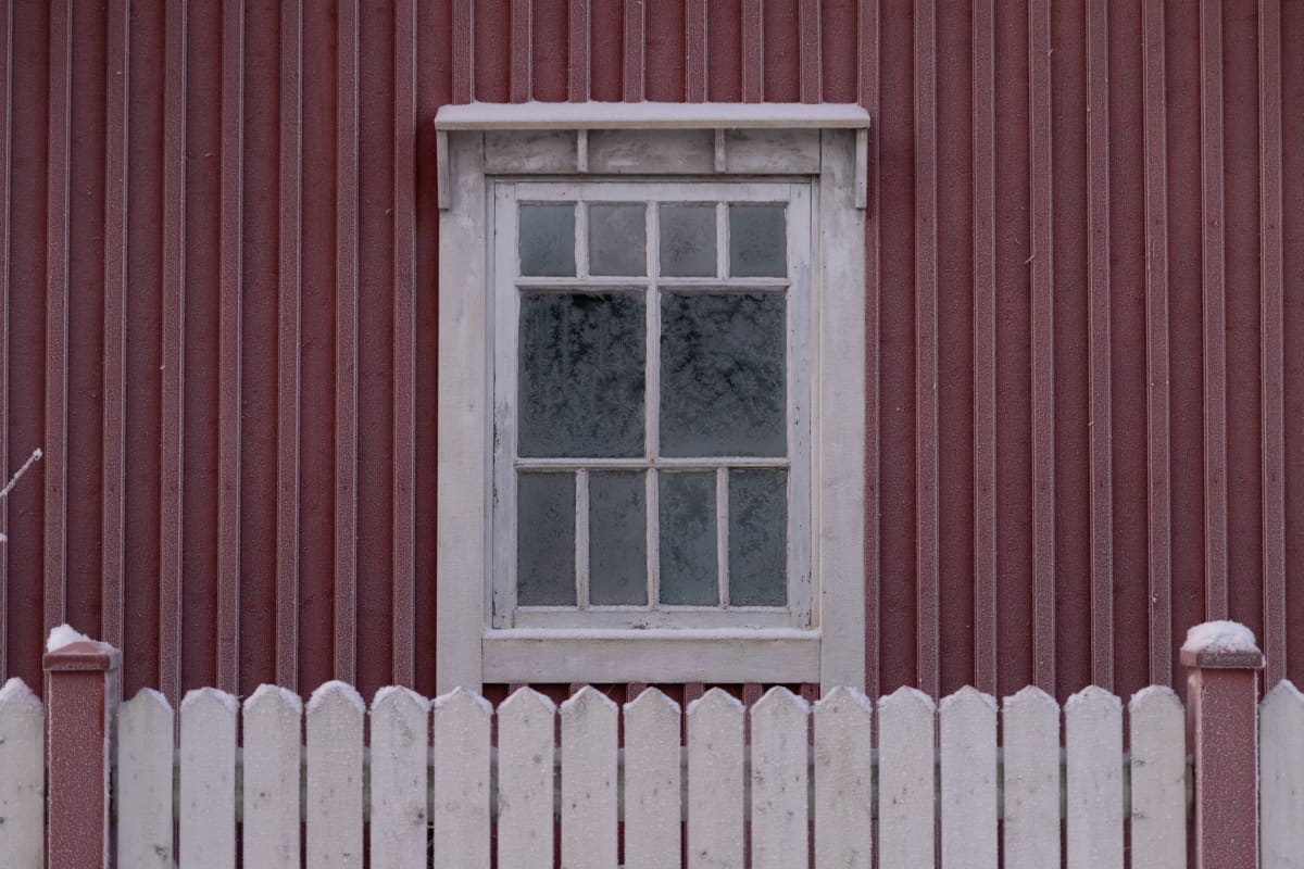 Punaisen puutalon seinä ja ikkuna huurussa.