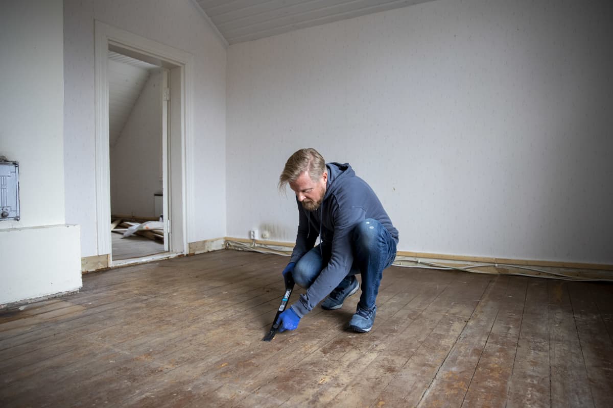Hannu Tylli on kyyristynyt irroittamaan työkalulla nauloja lautalattian pinnasta vanhan talon tyhjässä huoneessa.