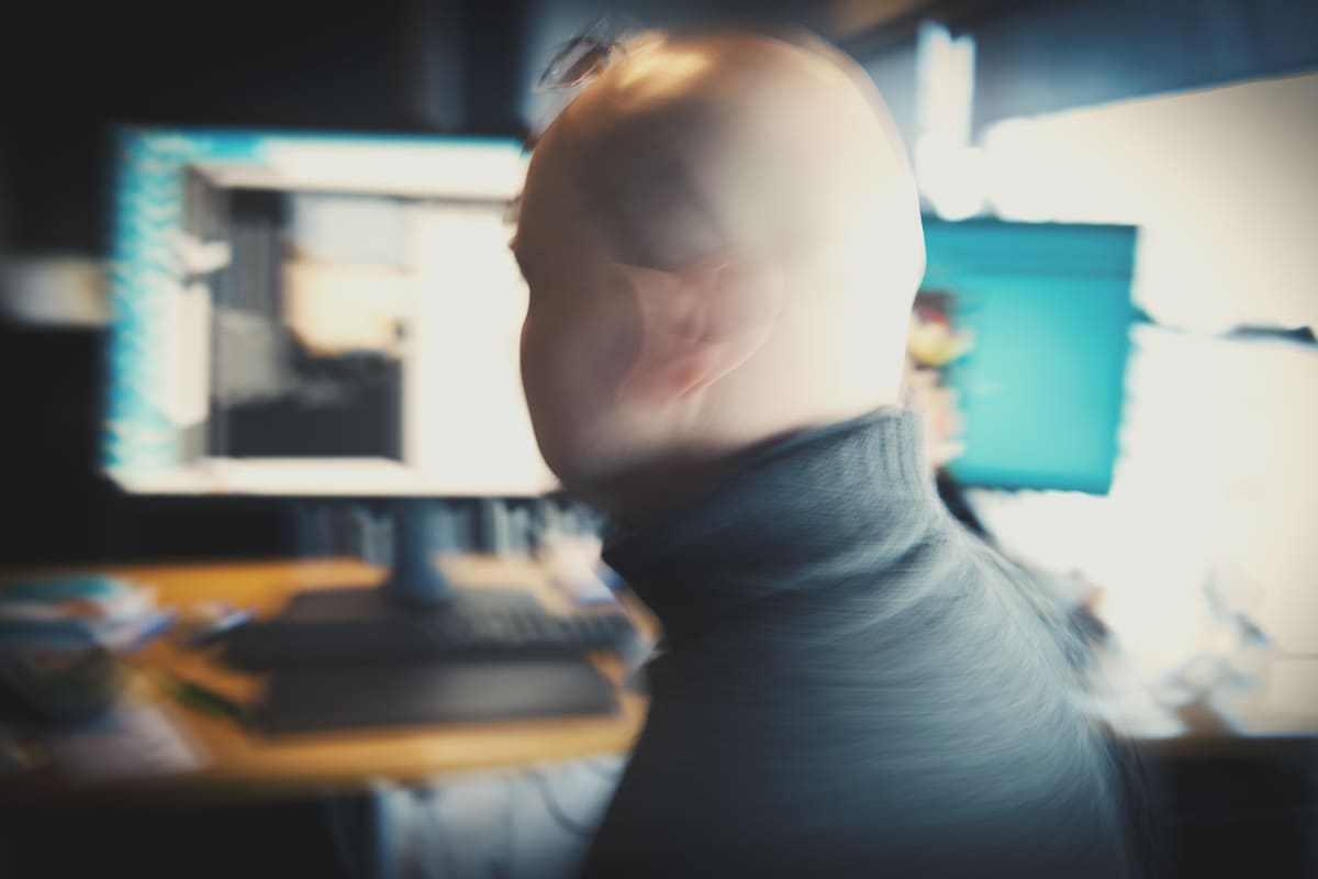 Mies tietokoneen monitorien edessä liikkeestä epäselvänä hahmona.