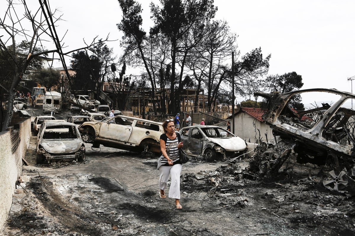 Nainen kävelee  maastopalojen tuhoamien autojen ohitse Ateenassa.