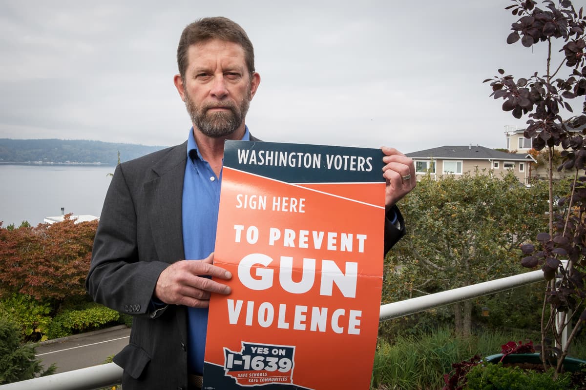 Mies katsoo kameraan käsissään juliste, jossa lukee "sign here to prevent gun violence".