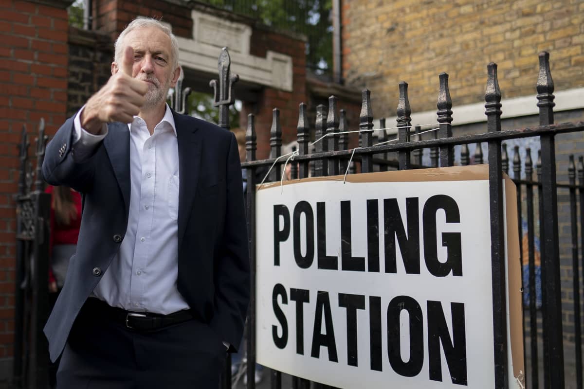 Jeremy Corbyn näyttää peukkua. Vieressä äänestyspaikan osoittava kyltti.