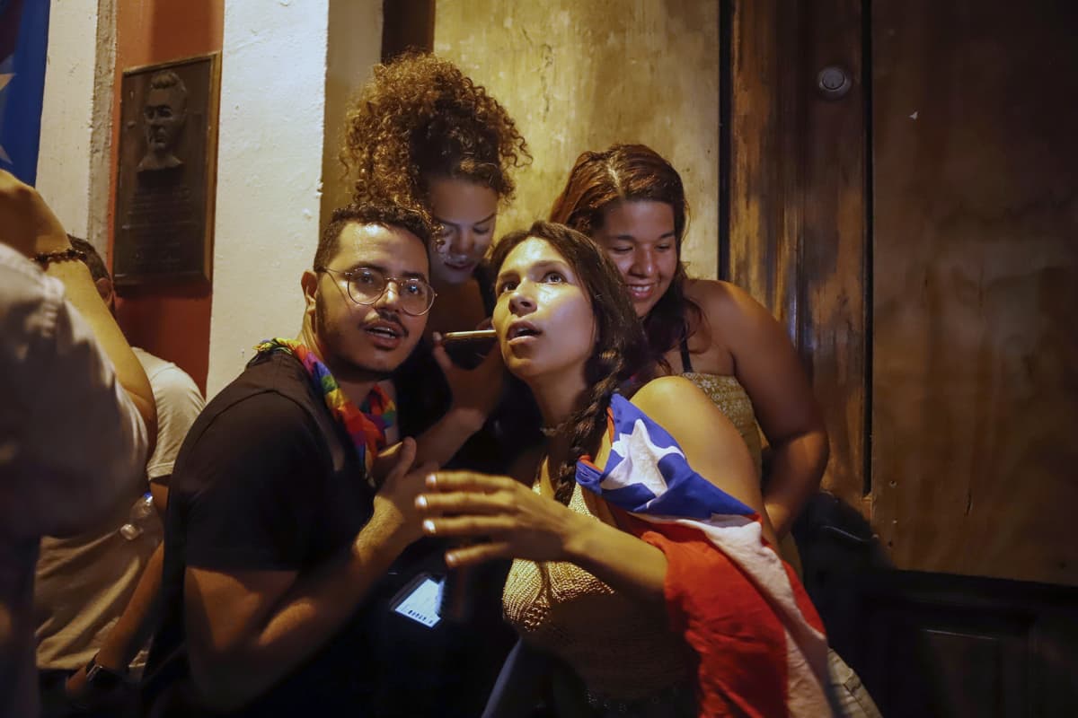 Neljä nuorta ihmistä kuuntelee Puerto Ricon kuvernöörin Ricardo Rossellon ilmoitusta kännykästä La Fortalezan vieressä, San Juanissa, Puerto Ricossa, 24. heinäkuuta 2019.