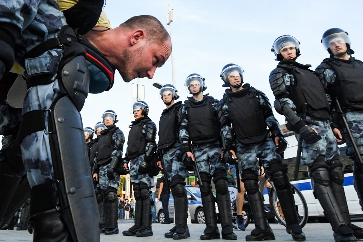 Poliisit tuijottavat pidätettyä mielenosoittajaa.