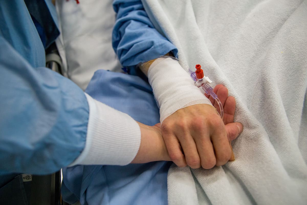 Henkilö tukee hoidossa olevaa potilasta pitämällä sitä kädestä kiinni.