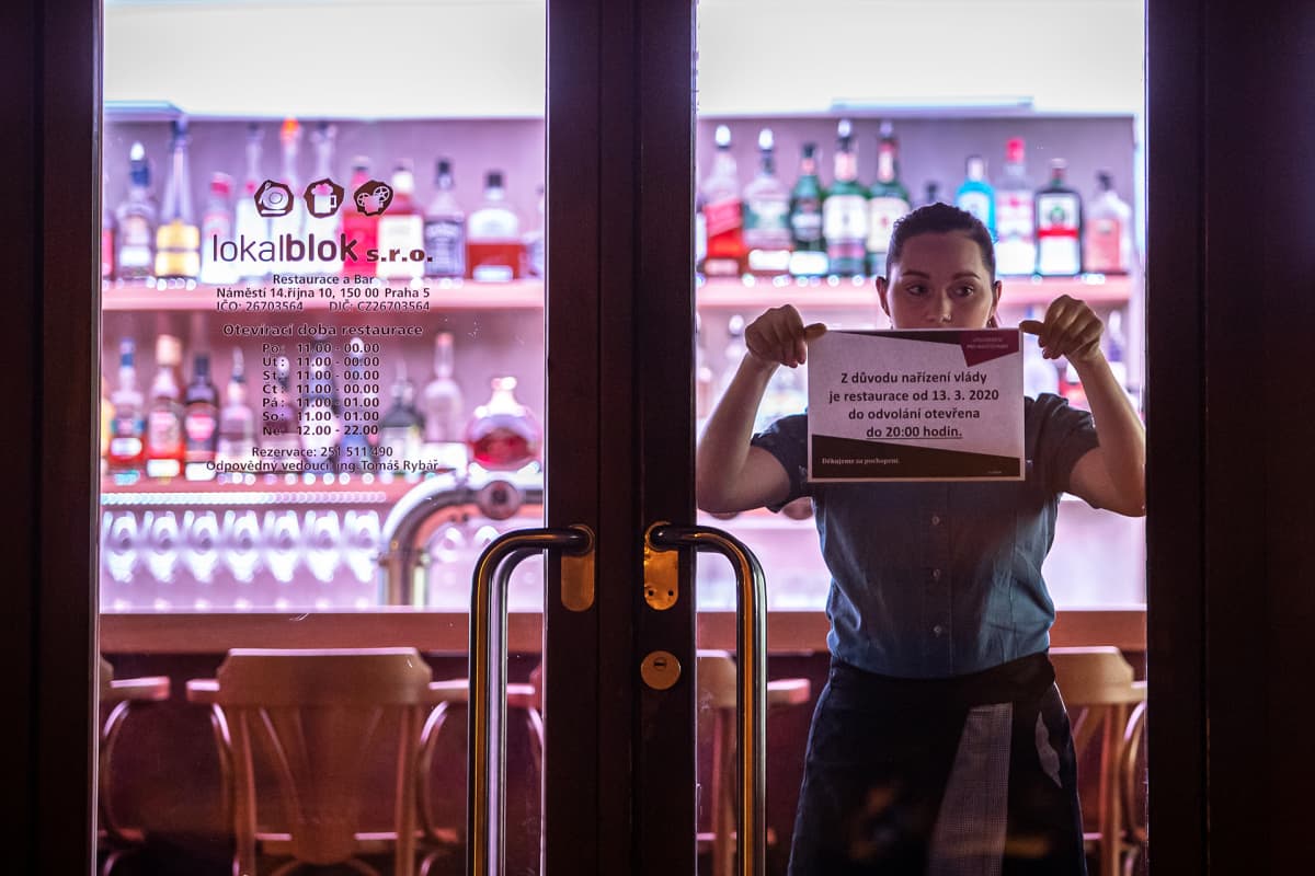 Tarjoilija kiinnittää ravintolan oveen ilmoitusta sulkemisesta Prahassa.