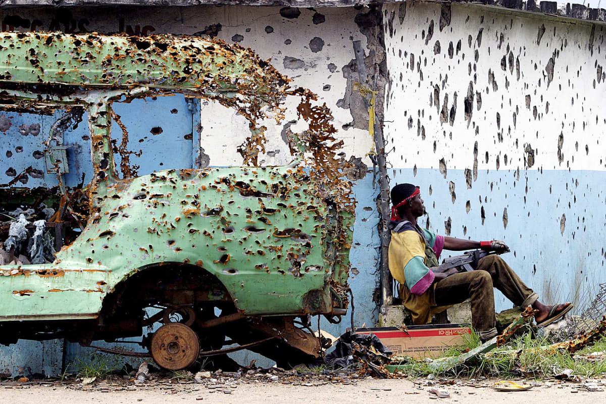LURD:n sissi istuu luodinreikiä täynnä olevan seinän vierellä Monroviassa Liberiassa.