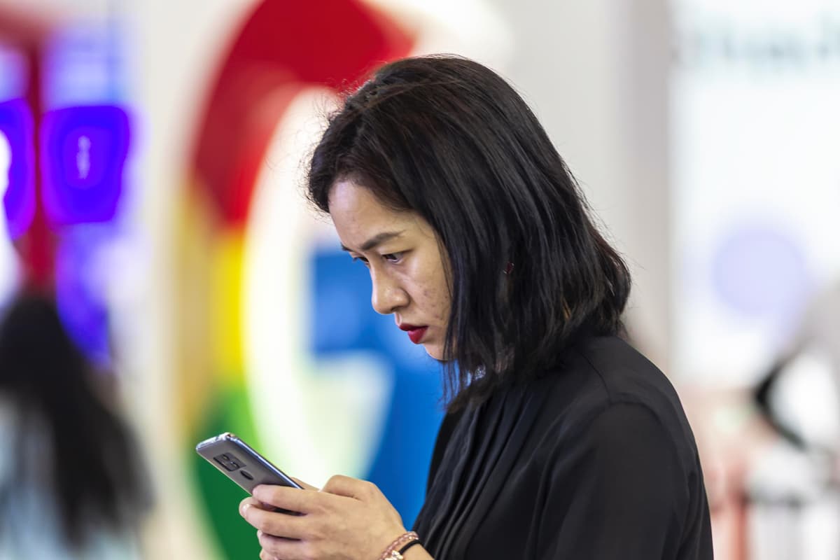 Nainen selaa puhelinta Googlen logon edustalla messuilla Guiyangissa Kiinassa