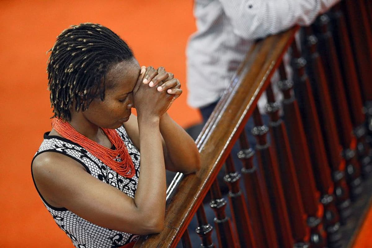nainen rukoilee kirkossa nojaten kaiteeseen
