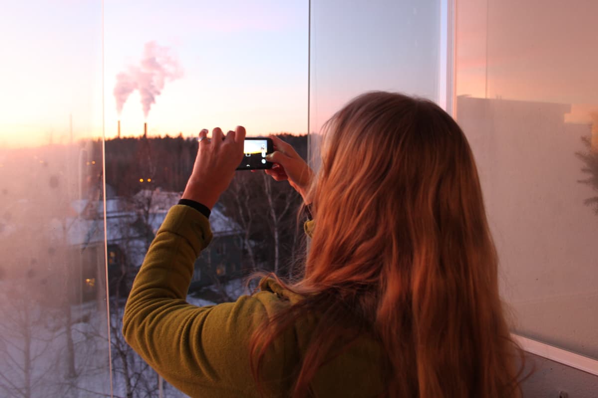 Nainen kuvaa parvekkeelta auringonlaskua kännykkäkameralla.