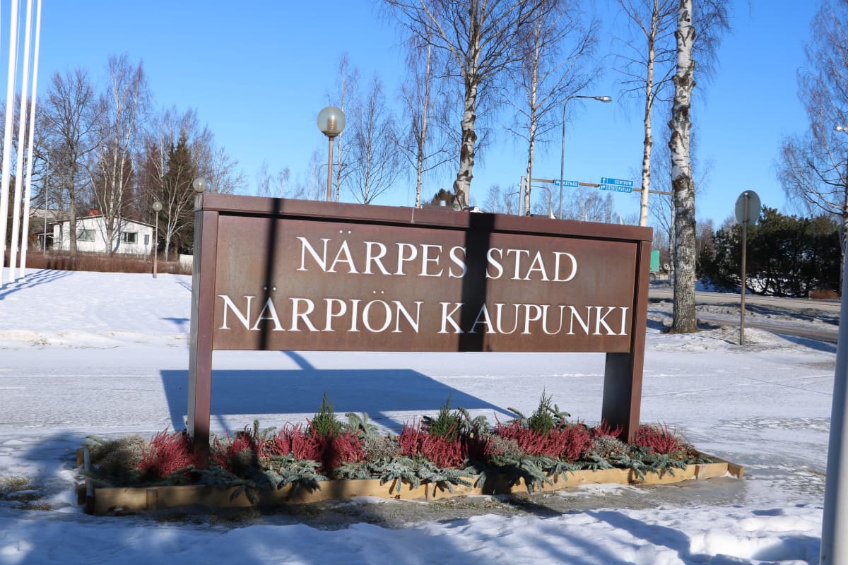 En skylt med texten Närpes stad står i en blomrabatt. Marken är täckt av snö.