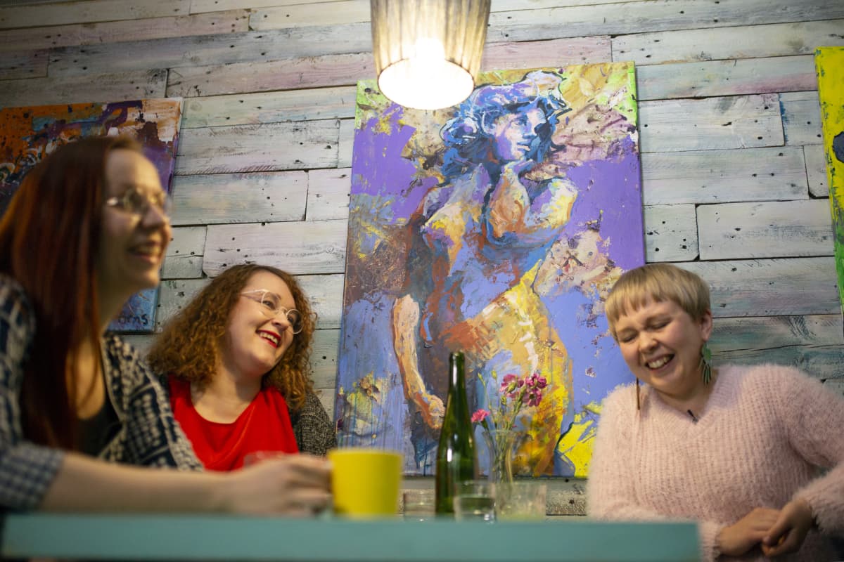 Jemina Viitala (vas), Mertta Hätinen ja Laura Liimatainen Helsingin Lauttasaaressa sijaitsevassa Maker´s -kahvilassa. Taustalla Simon Arnsin tekemä Havis Amanda -maalaus.
