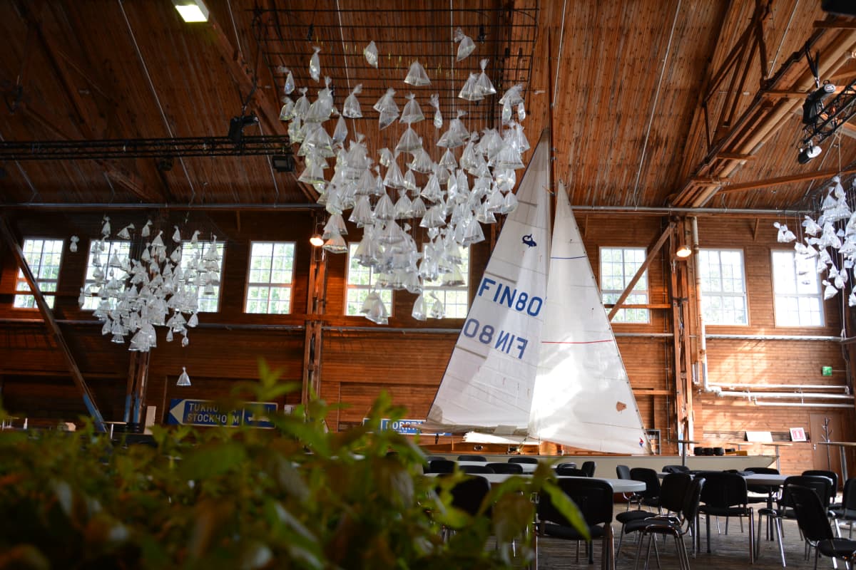 En stor festsal med en segelbåt med hissade segel. I taket hänger konstverk som ser ut som mängder av små segelbåtar.