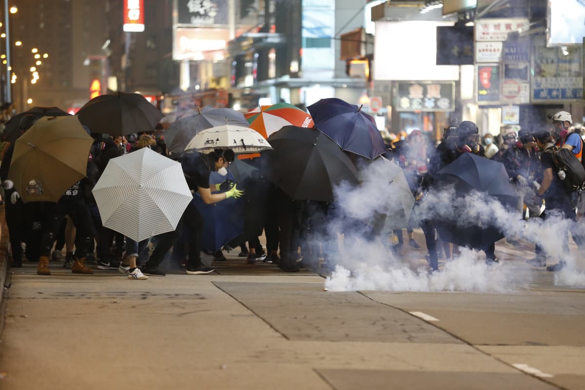 Ihmisjoukko suojautuu sateenvarjojen taakse kyynelkaasulta.