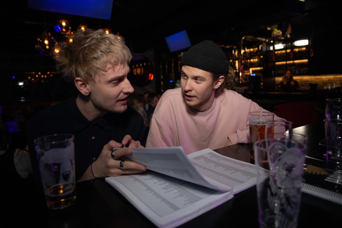 Noin kaksikymmentävuotiaat Olavi Tanttu ja Arttu Porkka selaavat karaokebaarissa listaa saatavilla olevista musiikkikappaleista.