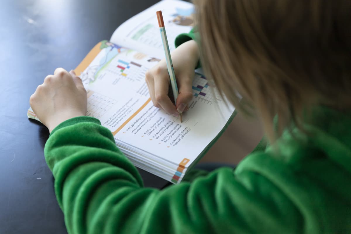 Lapsi tekee matematiikan tehtäviä kirjaan kotona.