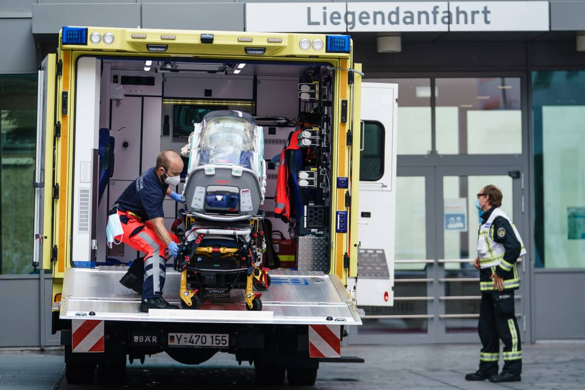 Mies työntää läpinäkyvällä kuvulla varustettua eristysyksikköä sisään ambulanssin takaovesta.