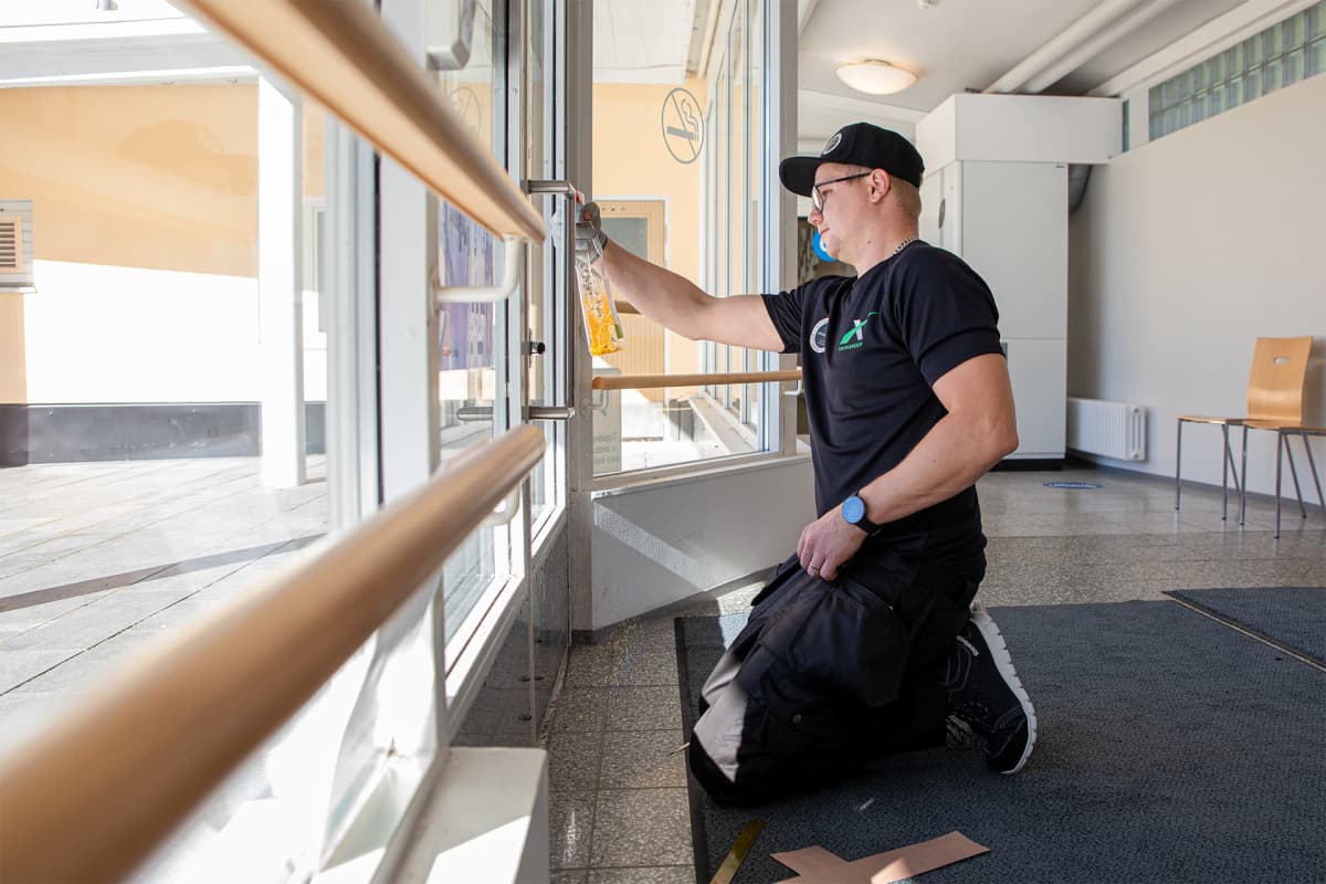 Henri Kaipio puhdistaa ovenkahvan ennen covidsafe tarrapinnoitteen asentamista.