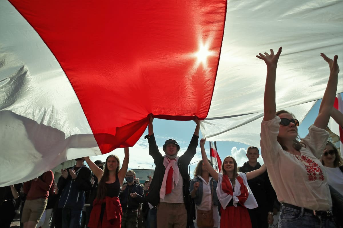 Mielenosoittajat kannattelevat punavalkoista Valko-Venäjän lippua. Aurinko loistaa lipun läpi.