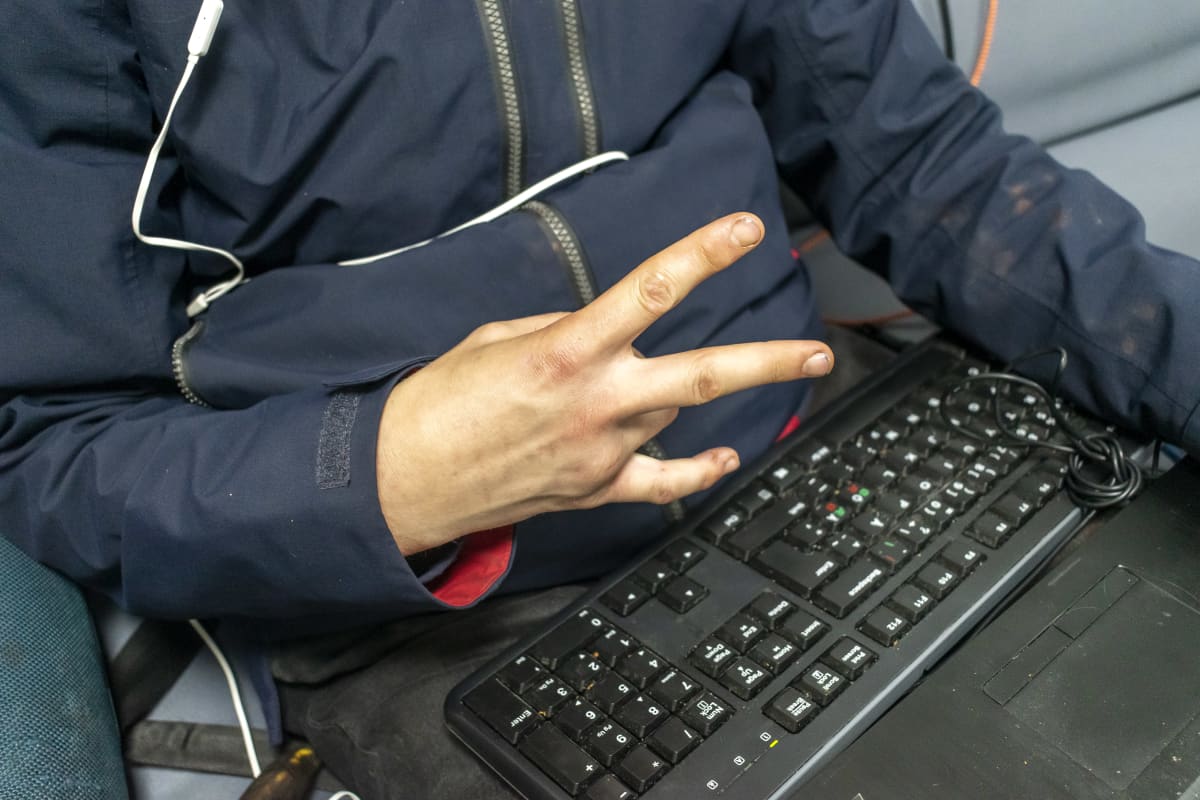Mies näyttää käsimerkkiä tietokoneen näppäimistö sylissä.