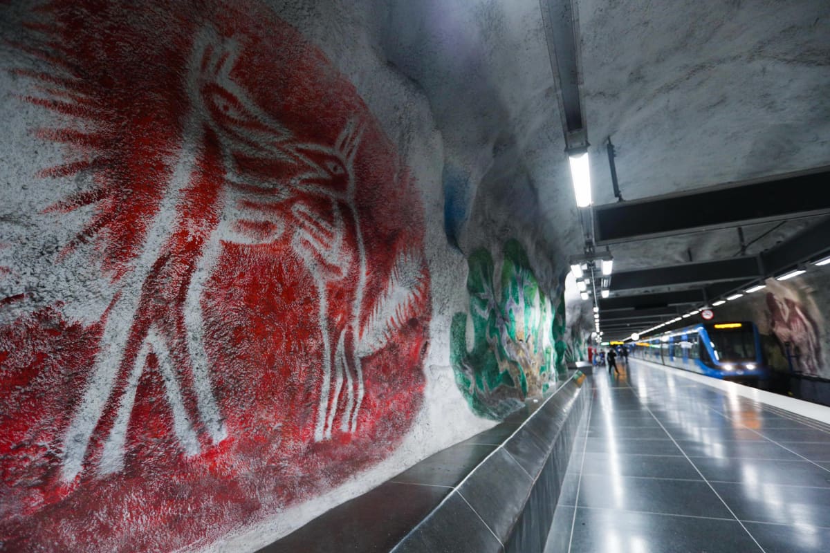 Näkymä Tenstan metroaseman laiturilta. Kuvassa iso seinämaalaus ja asemalla seisova metrojuna.